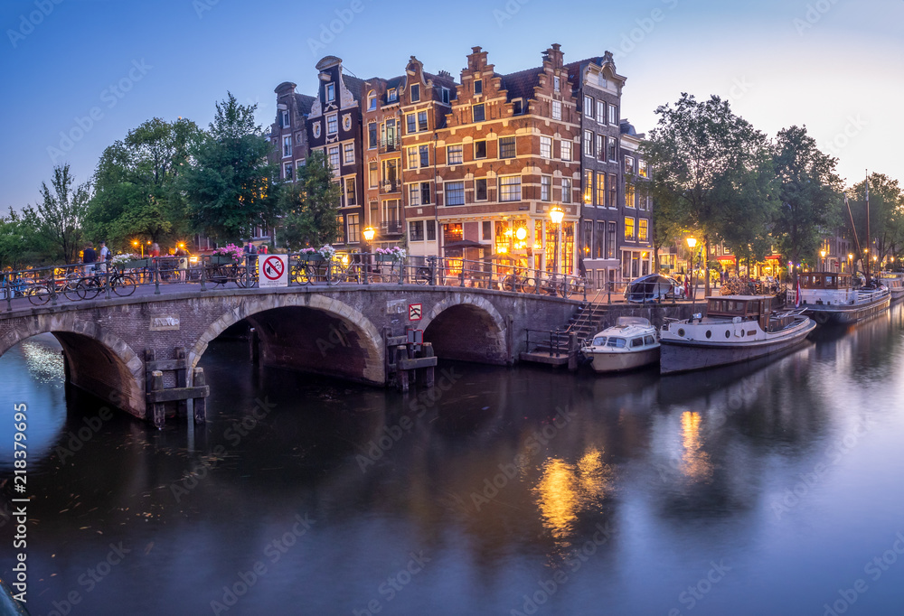 Fototapeta premium Amsterdam canal, bridge and typical houses, boats and bicycles during evening twilight blue hour, Holland, Netherlands.