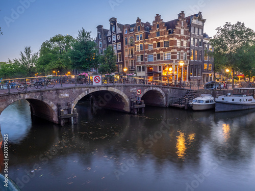 Amsterdam canal, bridge and typical houses, boats and bicycles during evening twilight blue hour, Holland, Netherlands.