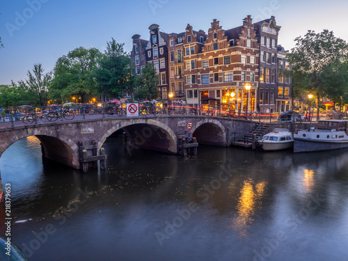 Amsterdam canal, bridge and typical houses, boats and bicycles during evening twilight blue hour, Holland, Netherlands.