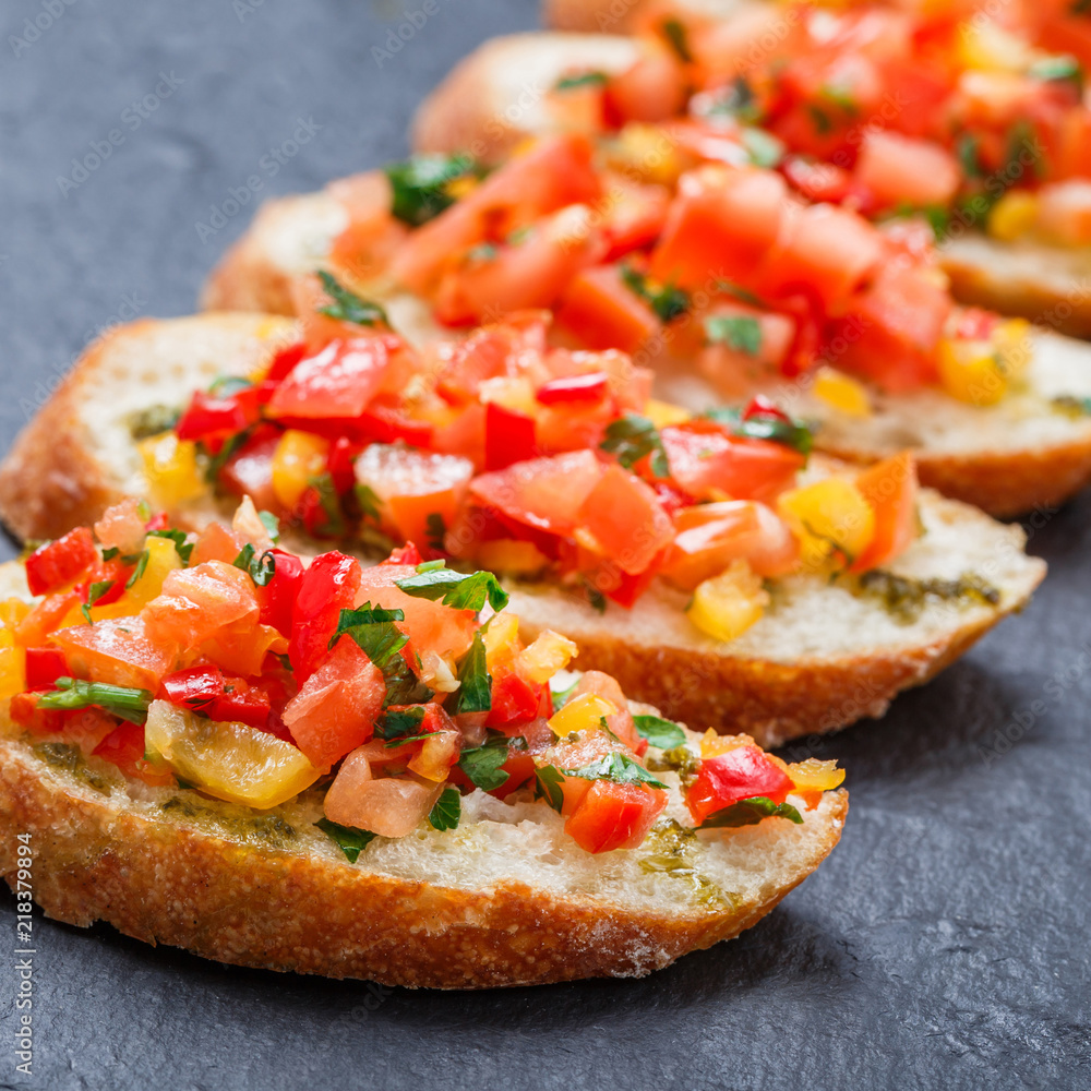 Appetizer bruschetta with chopped vegetables on ciabatta bread on stone slate background close up. Delicious snacks, sandwiches, crostini, canape, antipasti on party or picnic time