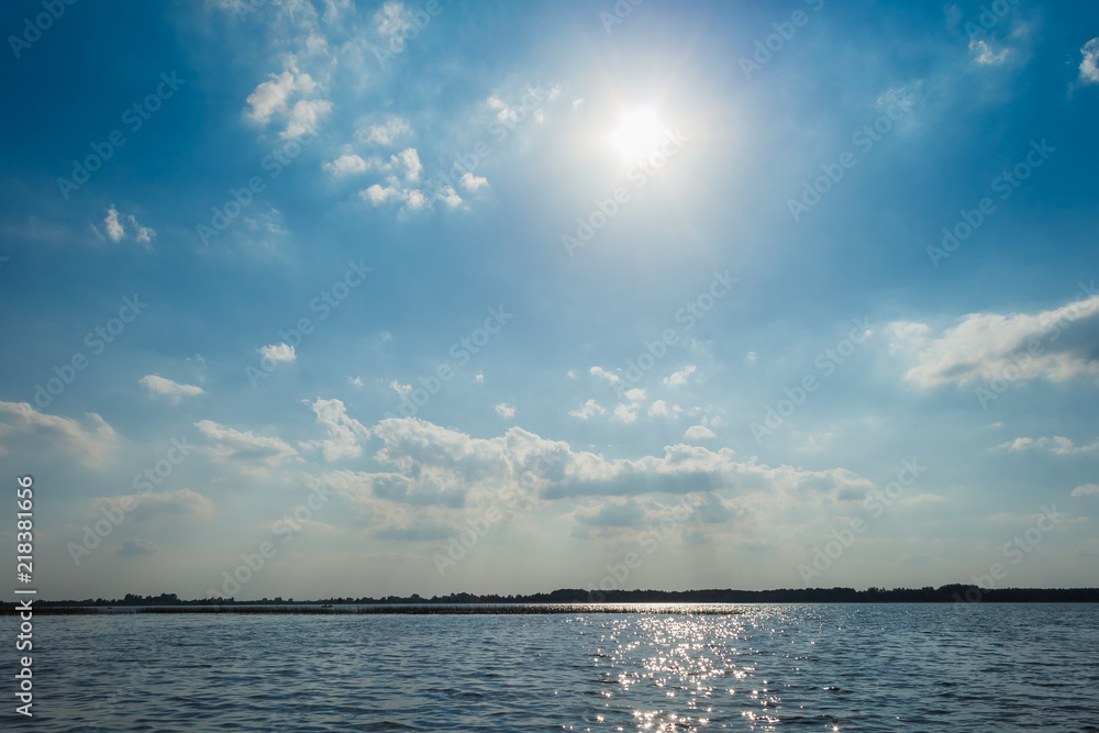 Waves and glare on the surface of the water. Lake on a sunny day with blue sky and white clouds