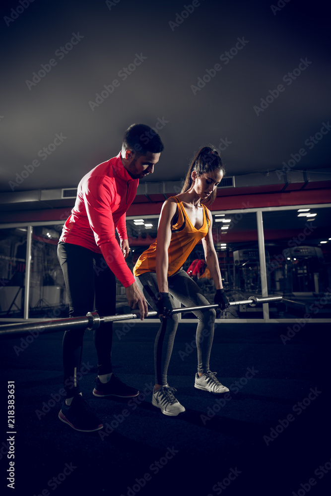Fototapeta premium Young fit female is doing dead lifts with a help of her coach.