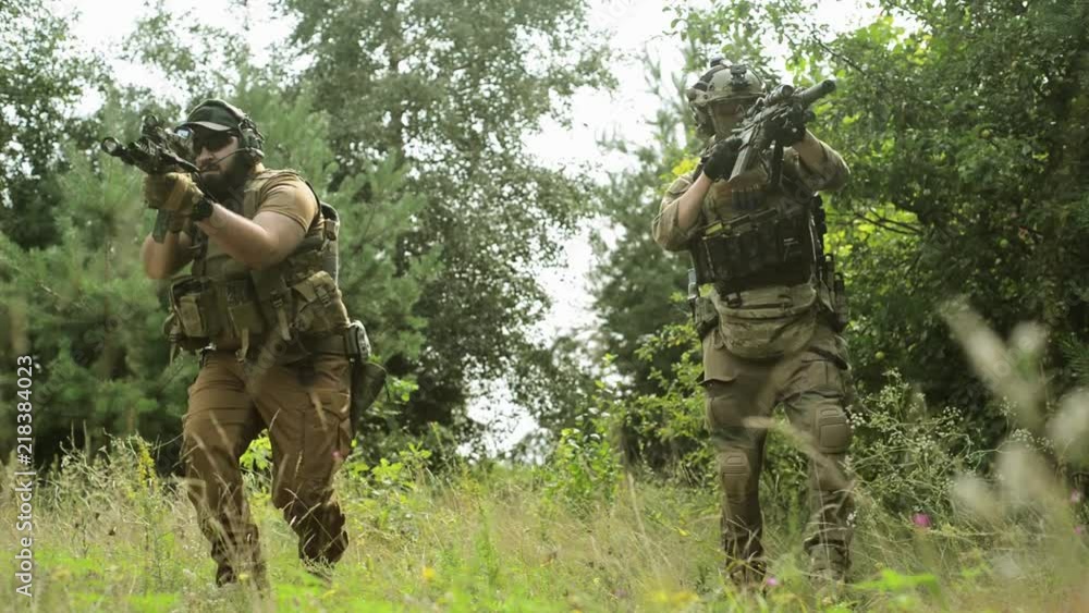 Close up airsoft men in ammunition go with machinegun. Move on camera, view from down Close up airsoft men in ammunition go with machinegun. Move on camera, view from down