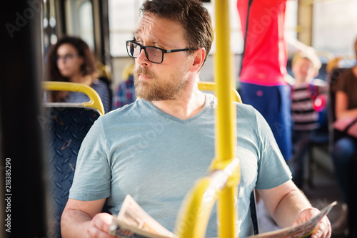 Serious man is holding newspapers in his hand while sitting in a bus.