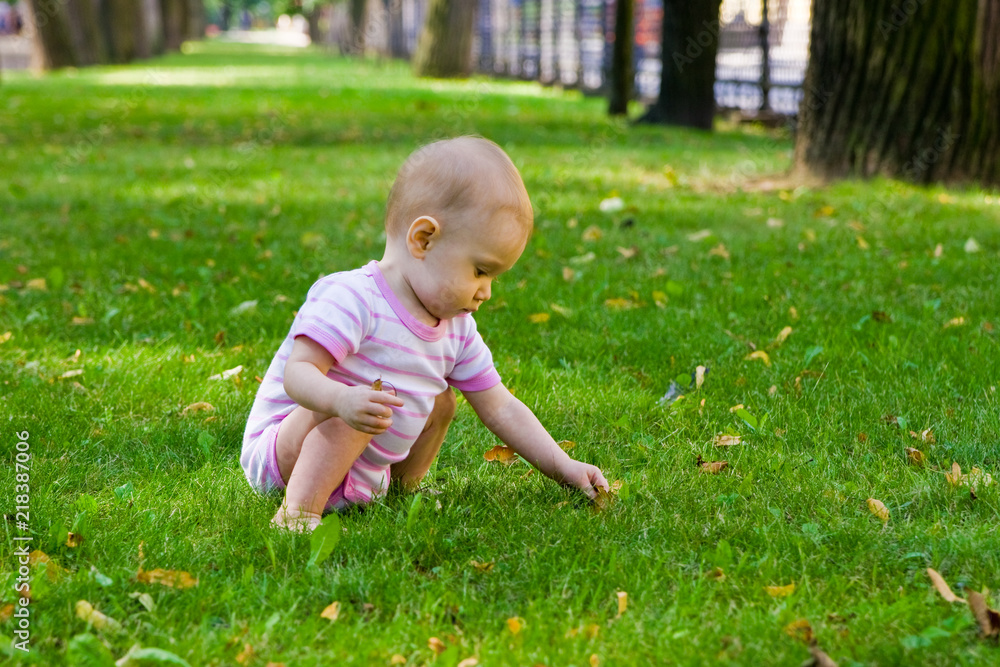 baby girl collecting leaves lying on grass in park baby girl collecting leaves lying on grass in park