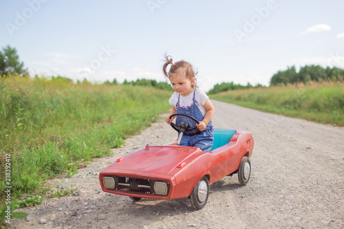 A sweet girl runs a children's car on the road in the summer