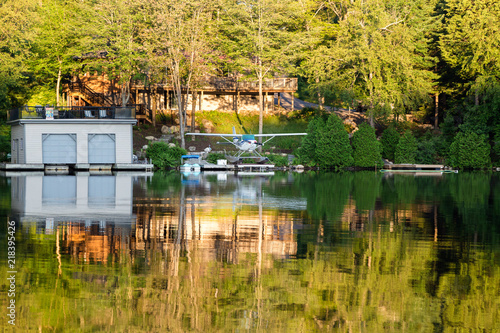 A small Cessna 182 float plane on a dock at a lakeside cottage at dawn.