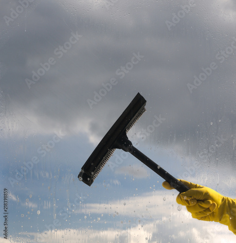 Hand in protective glove cleaning window on background of cloudy sky