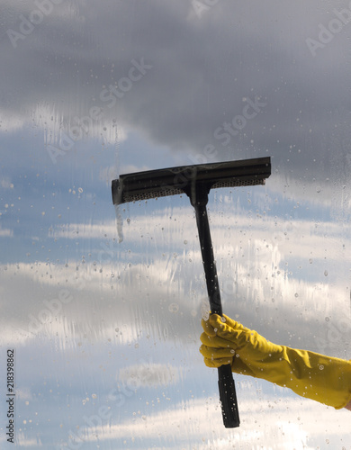 Hand in protective glove cleaning window on background of cloudy sky