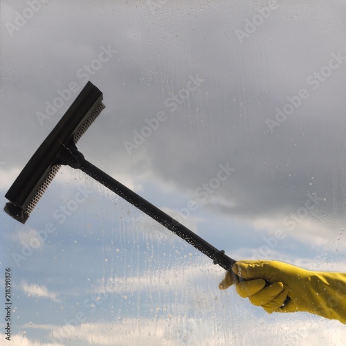 Hand in protective glove cleaning window on background of cloudy sky