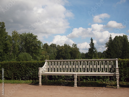 vintage white bench in the Park on the background of trimmed bushes, trees and cloudy sky