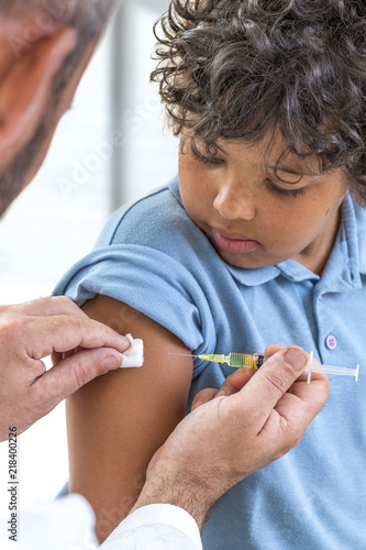 Vaccination. Young boy receiving vaccination immunisation by professional health worker, kid looking on shoulder