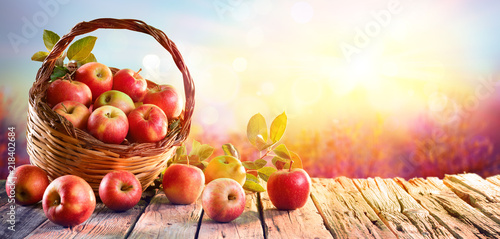 Fototapeta Czerwone jabłka w koszu na drewnianym stole o zachodzie słońca XXL