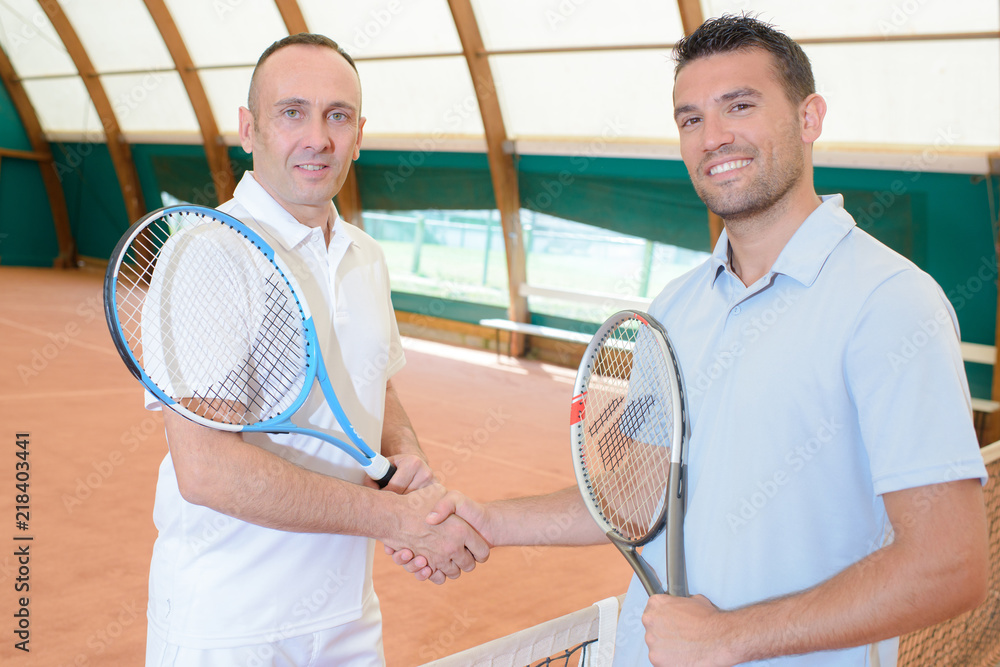 Two men shaking hands on tennis court - obrazy, fototapety, plakaty 