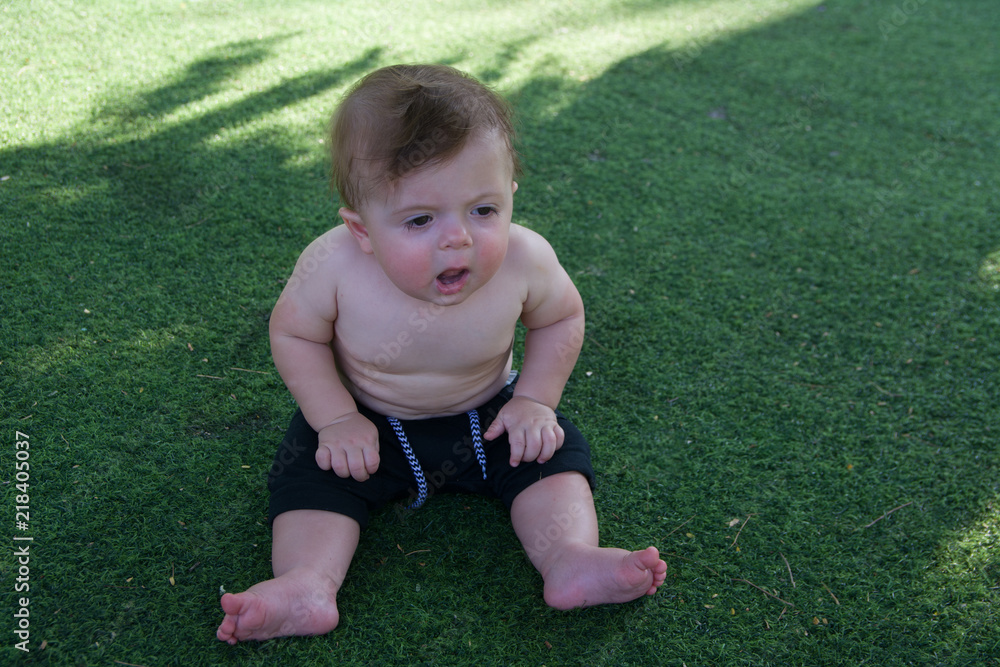 Happy adorable baby boy sitting on the grass and laughing in summer day. Happy smile, 9 months old. Happy adorable baby boy sitting on the grass and laughing in summer day. Happy smile, 9 months old.