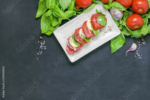 .Caprese salad made of sliced fresh tomatoes, mozzarella cheese and basil served on a white plate on a black backgroundTraditional Italian food photo