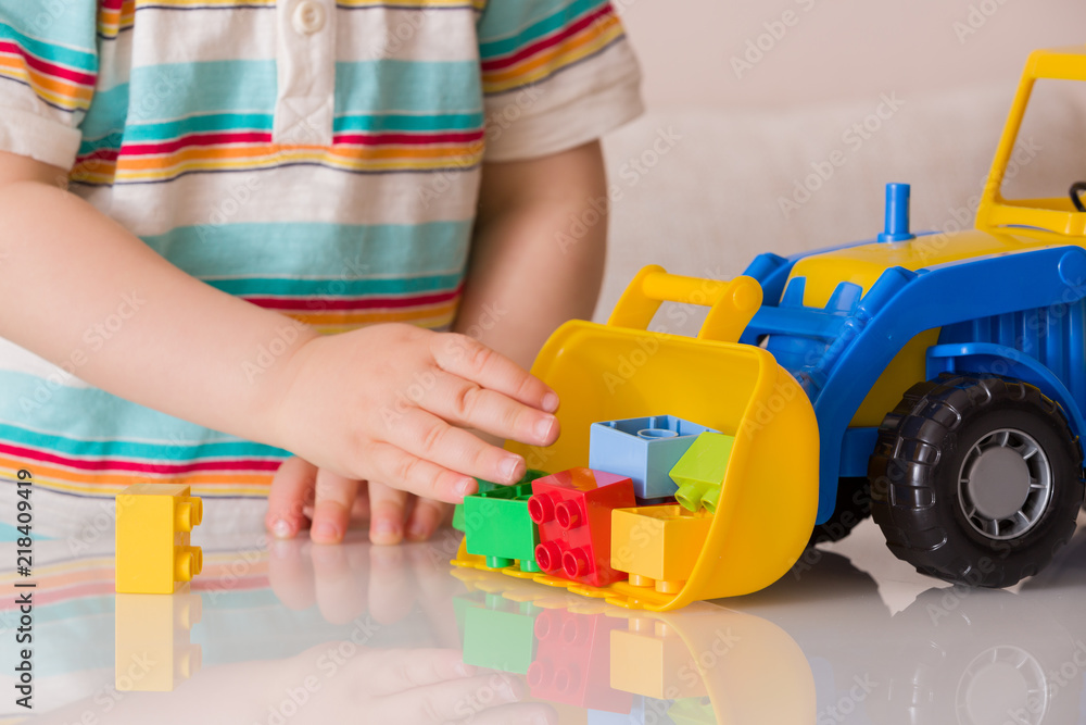 Closeup of toddler boy playing with colorful plastic bricks or details and a toy tractor. A child plays with a car in a nursery or preschool.