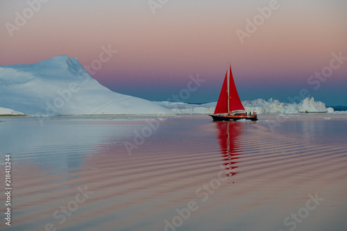Greenland after midnight glow light iceberg mirror panorama with red sail ship 
