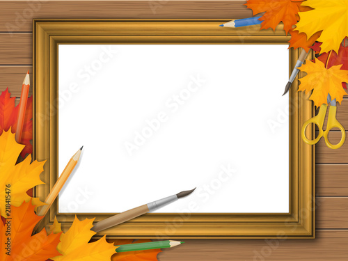 Golden vintage picture frame with autumn leaves and art supplies on wooden background. With place for text, pictures or advertisements. Fine art.