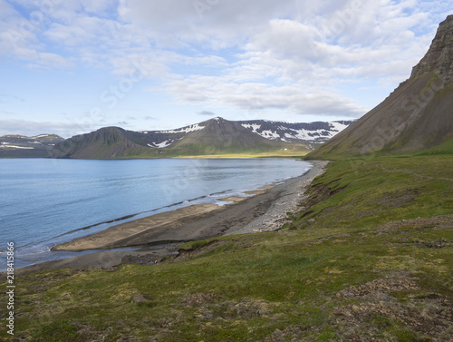 Northern summer landscape, sand bech with view on beautiful snow covered cliffs and Alfsfell mountain, Hloduvik cove in Hornstrandir, west fjords, Iceland, green meadow, blue sky background photo