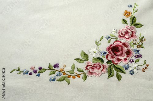 Embroidered corner with a bouquet of pink- red roses with small multicolored flowers and bright berries on white cotton fabric