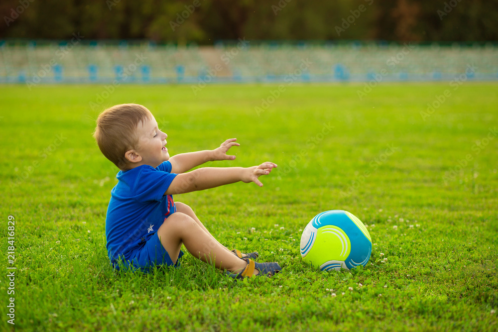Little funny boy on stadium play football in summer day