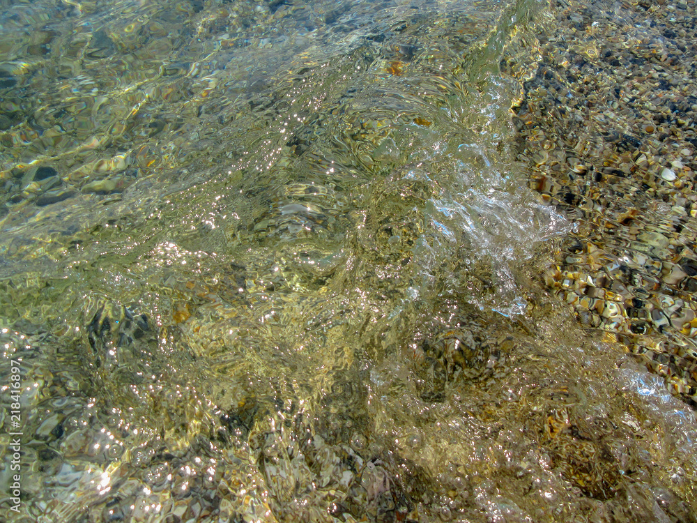 Texture from nature. Whirlpool of transparent sea water over multicolored pebbles.