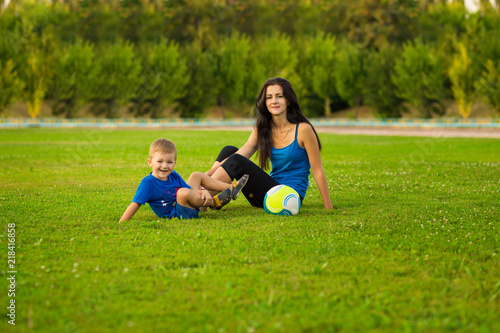 Mother and little son playing ball on grass in summer park