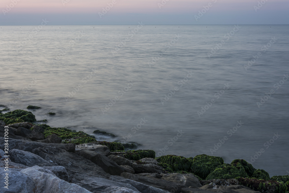 The infinity horizon above the sea. The stone beach with moss and eyelashes. The waves flow to the coastline. Morning atmosphere before sunrise.