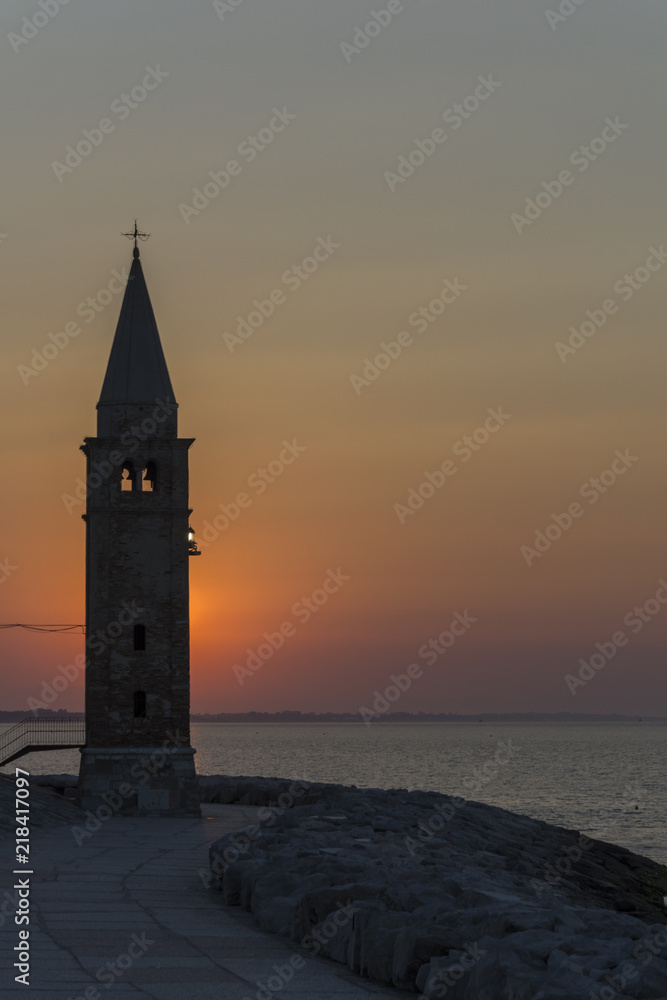 The tower in front of sunrise over the sea on the stone beach. Town Caorle.
