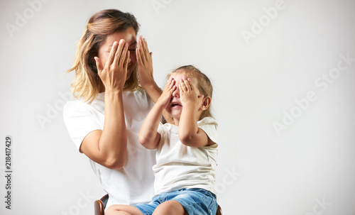 Little girl playing peekaboo game with her mother on white background with copy space. Woman and child are playing peek-a-boo and having fun. Parenthood and happy moments concept photo