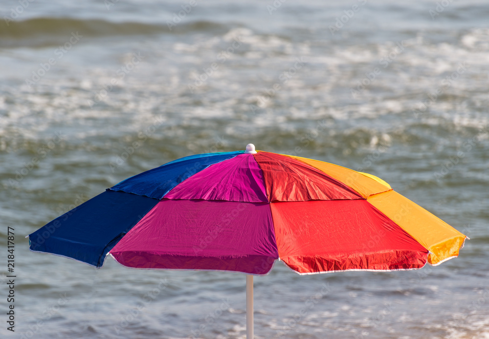 A colorful umbrella spread out on the beach on a beautiful sunny summer day with a rough sea.
