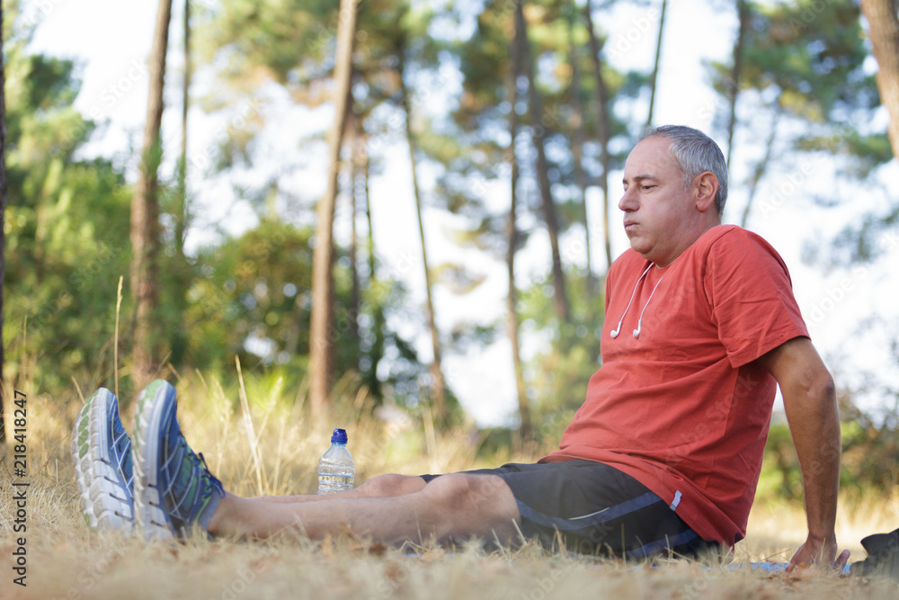 Naklejka premium Middle aged man sat on ground while out exercising
