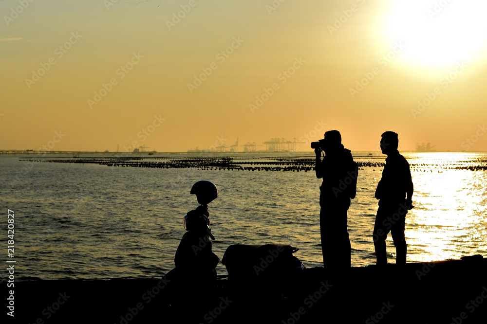 Silhouette of tourist take photo at sea with sunset sky