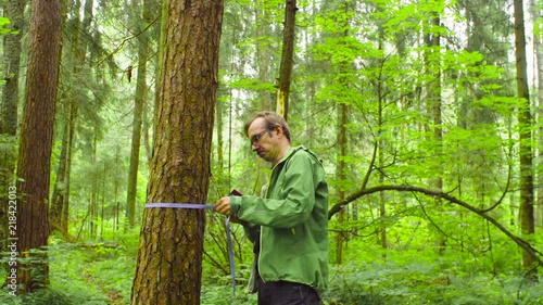 A scientist environmentalist exploring plants in a forest. He measuring a tree trunk