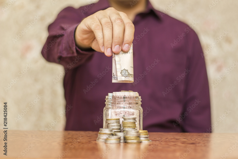 Youngman Putting Coin in Glass Jar Full of Coins, Saving Concept, Egyptian Pounds