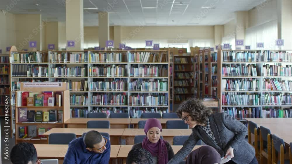 Tilt down of Caucasian female teacher giving a lecture to group of middle eastern migrants in library hall Tilt down of Caucasian female teacher giving a lecture to group of middle eastern migrants in library hall