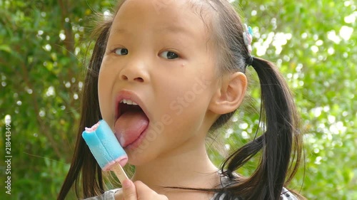 Little asian girl eating ice cream in park

