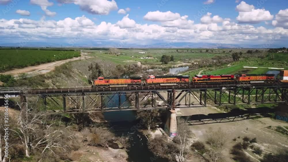 Wide aerial shot of a train transporting shipping containers on a bridge passing over the San Joaquin River on a sunny day with blue skies and white clouds with green agriculture landscape Wide aerial shot of a train transporting shipping containers on a bridge passing over the San Joaquin River on a sunny day with blue skies and white clouds with green agriculture landscape