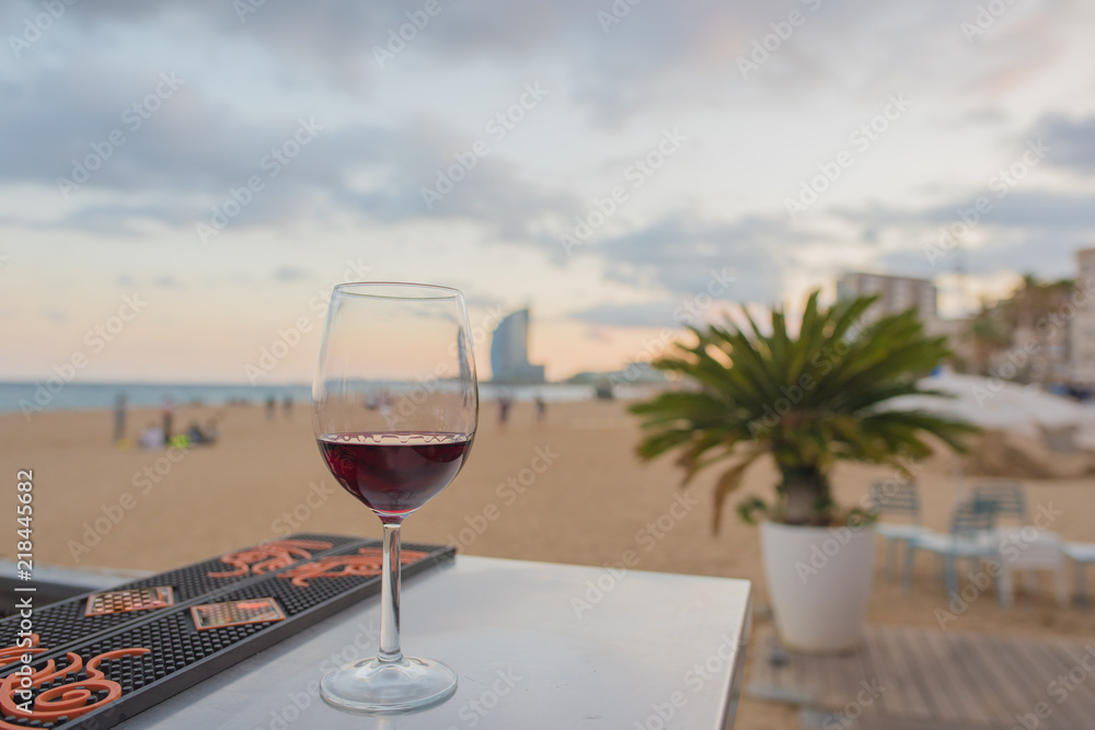 A glass of red wine on a bar overlooking the beach in Barcelona, Spain at sunset. Concept of a relaxing, blissful vacation.