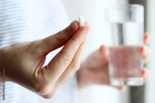 white pill and a glass of water in female hands. health concept photo