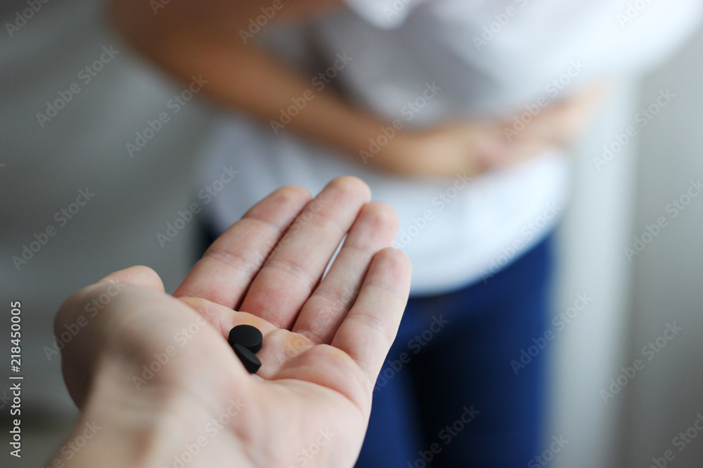 activated charcoal tablets in male hand, offering the sick girl. Giving pills to the patient. Light background. The concept of health