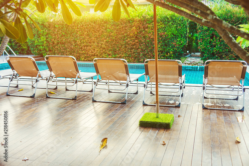 Rear view of sun loungers on wooden decks at the side of swimming pool. For relaxation and recreation in hotel resort. photo