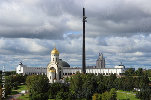 Moscow, Russia - day view to the Park Pobedy at poklonnaya hill - victory park, church, stele and monument meseum in autumn against green trees and overcast sky with heavy clouds