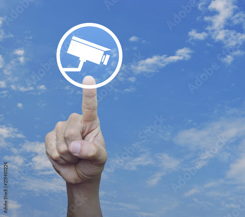 Hand pressing cctv camera flat icon over blue sky with white clouds, Business security and safety online concept