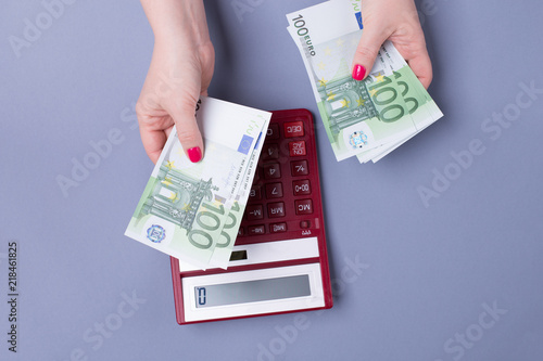 Female hands hold EURO bills and a calculator on a blue background - the concept of accounting.