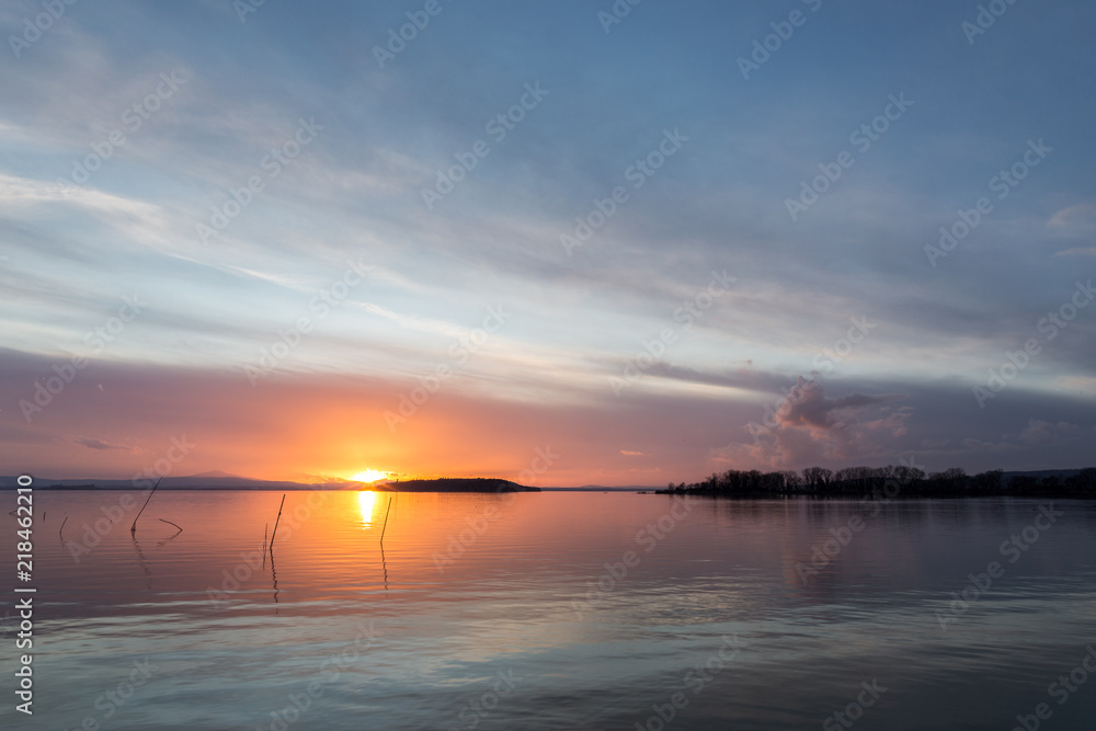 A shoot of a sunset over a lake, with beautiful warm colors and clouds and sun low on the horizon