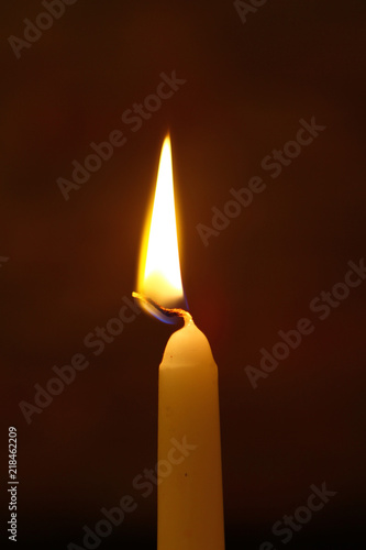 tiny paraffin burning candle with vivid flame on the heavy black background.