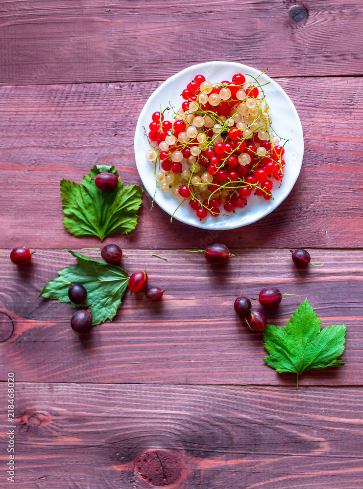 Berries of a currant, gooseberries on a saucer, leaves, on a natural wooden background Berries of a currant, gooseberries on a saucer, leaves, on a natural wooden background