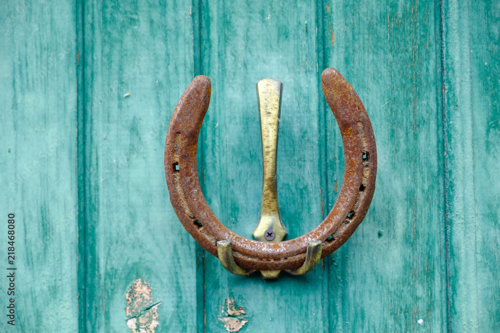 An old, rusty horseshoe hangs on a home-made hook against a wall of wooden boards painted with blue paint outdoors An old, rusty horseshoe hangs on a home-made hook against a wall of wooden boards painted with blue paint outdoors
